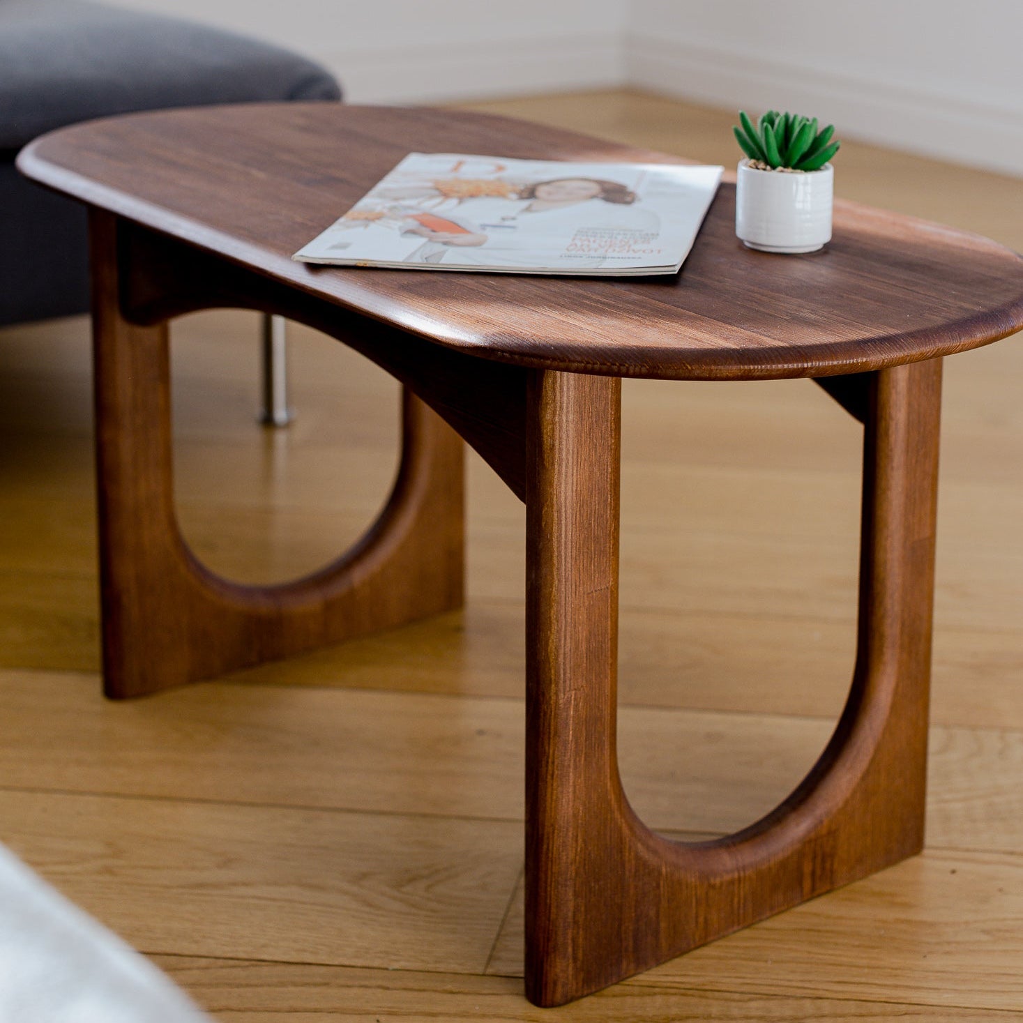 Wooden coffee table with a magazine and small plant on a wooden floor.