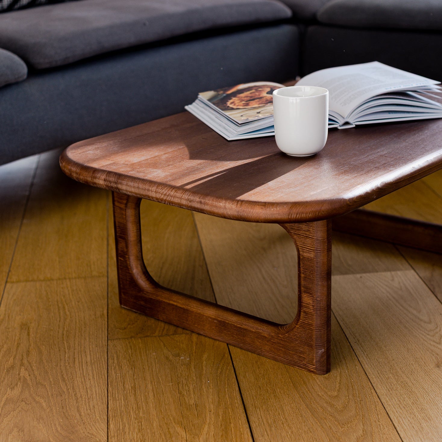 Wooden coffee table with a magazine and a white mug in a living room setting.