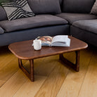 Gray sectional sofa with a wooden coffee table and magazines on a wooden floor.